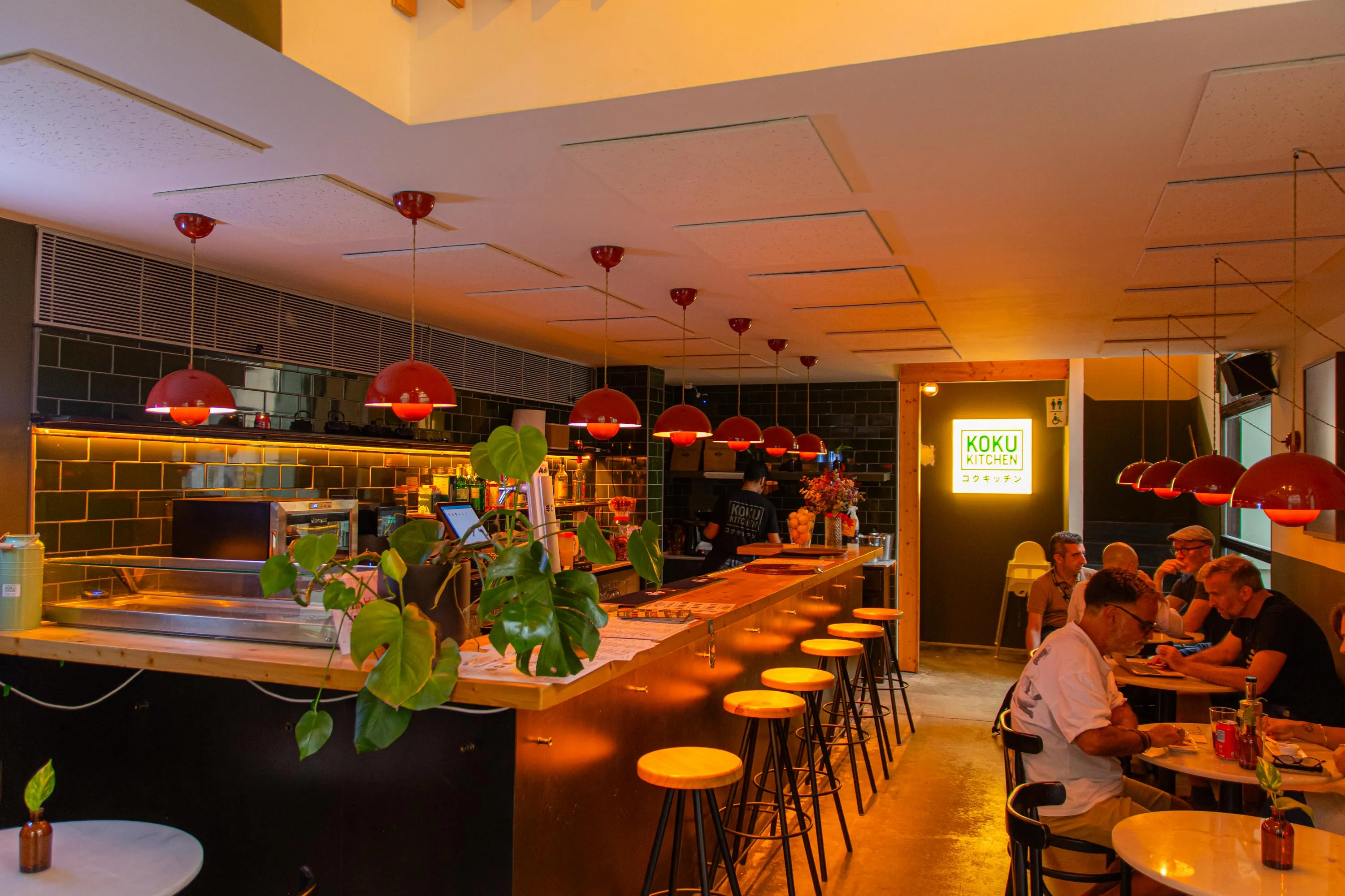 Guests at the tables beside the bar of Koku Kitchen Gràcia, with the lit Koku Kitchen sign at the back of the room