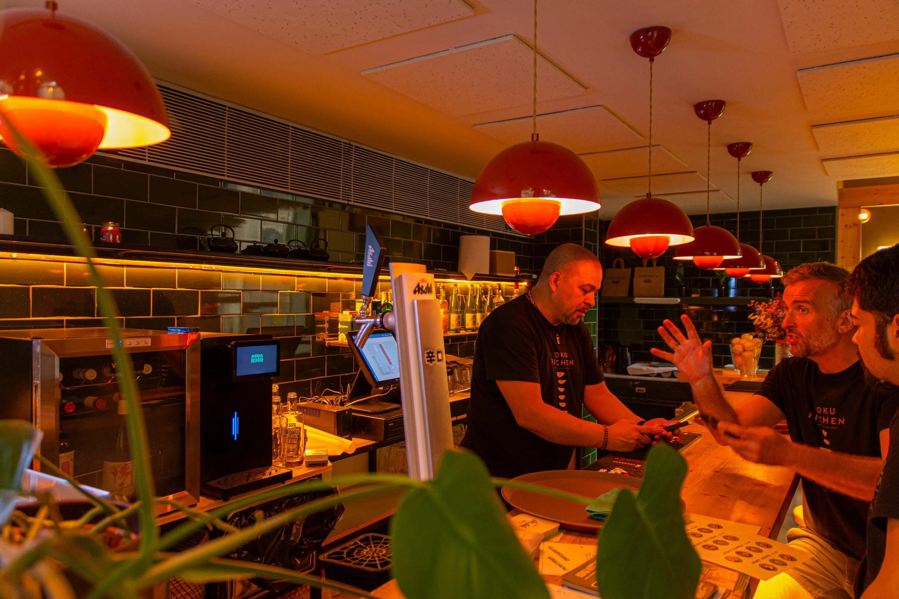 The team talking across the bar of Koku Kitchen Gràcia, beside the Asahi beer tap and under the red lamps