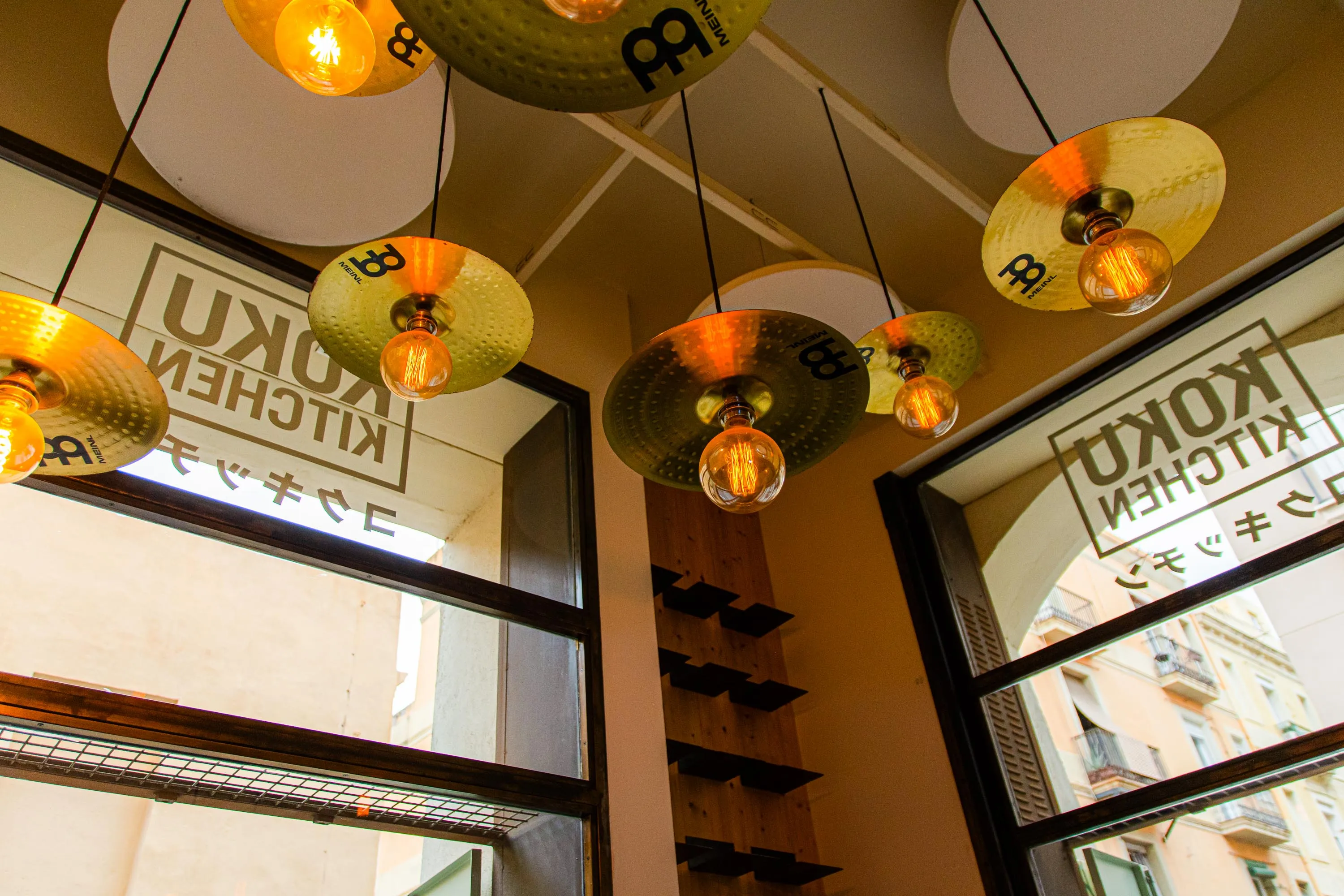 Lamps made from cymbals at Koku Kitchen Gràcia, with the restaurant's name on the windows behind them