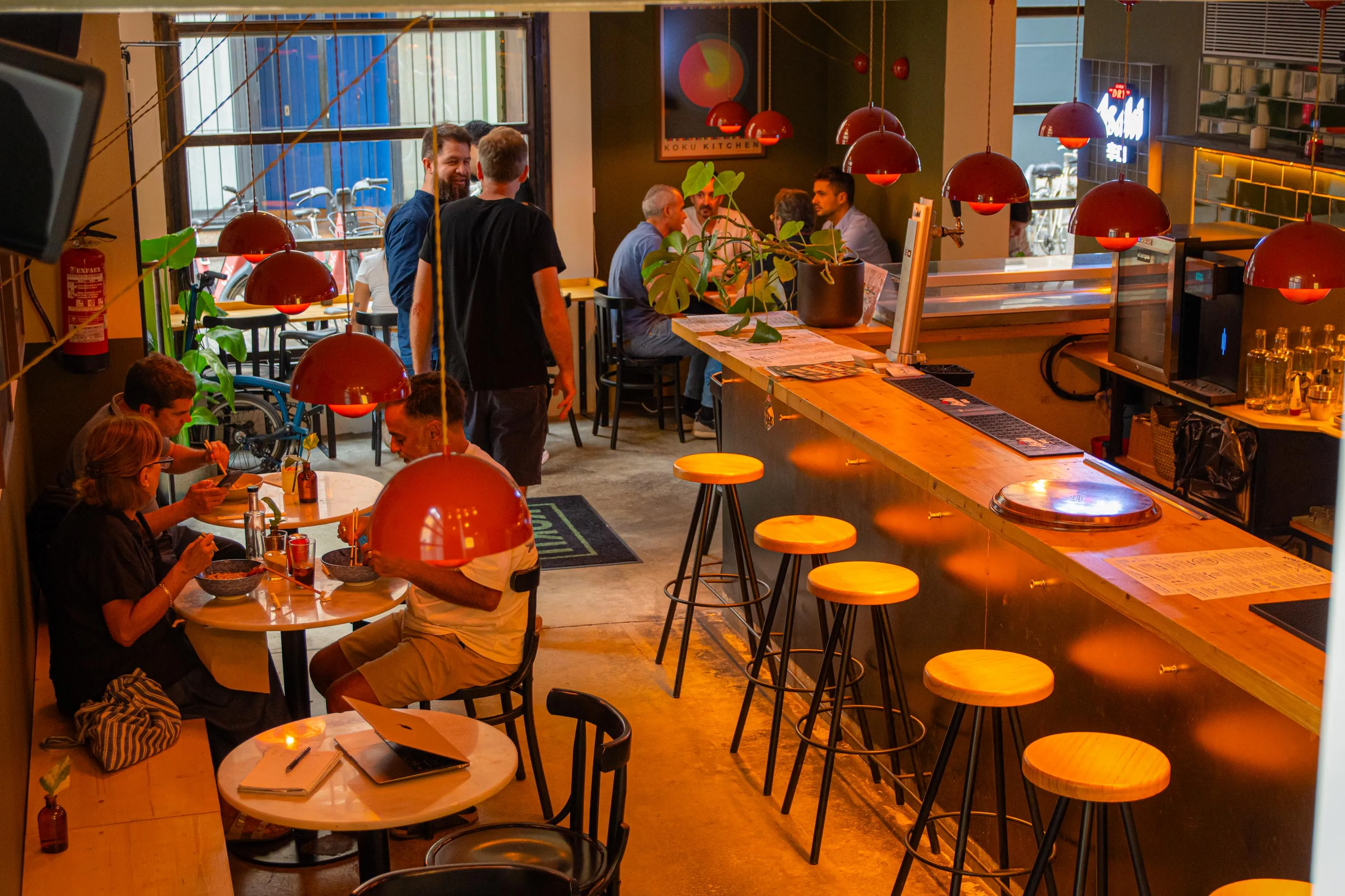 Guests eating at the round tables beside the bar of Koku Kitchen Gràcia, seen from above