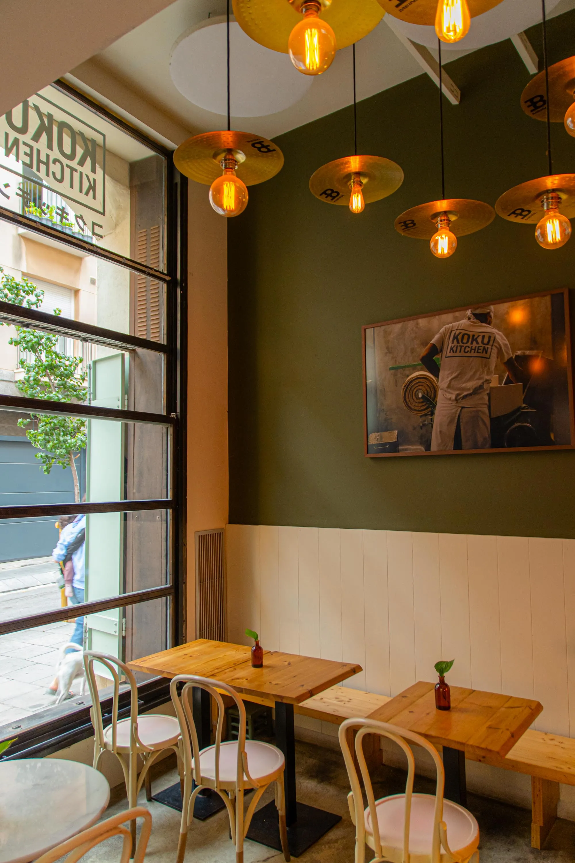Tables by the window of Koku Kitchen Gràcia, under lamps made from cymbals